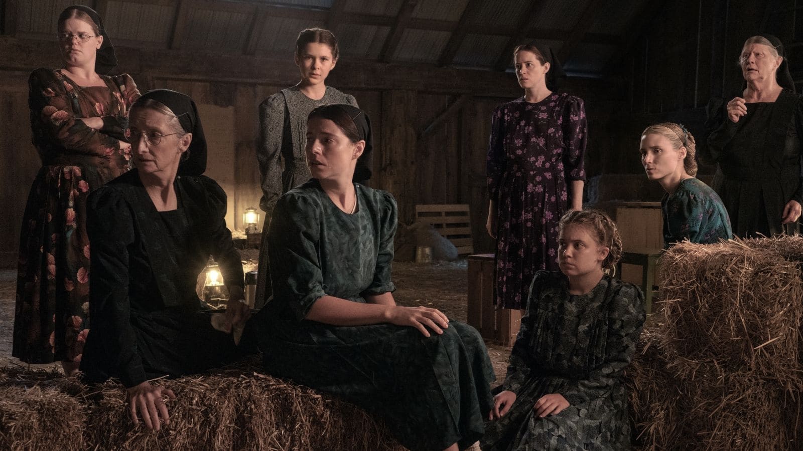 A group of eight women, varying in age, sit and stand amongst bails of hay.