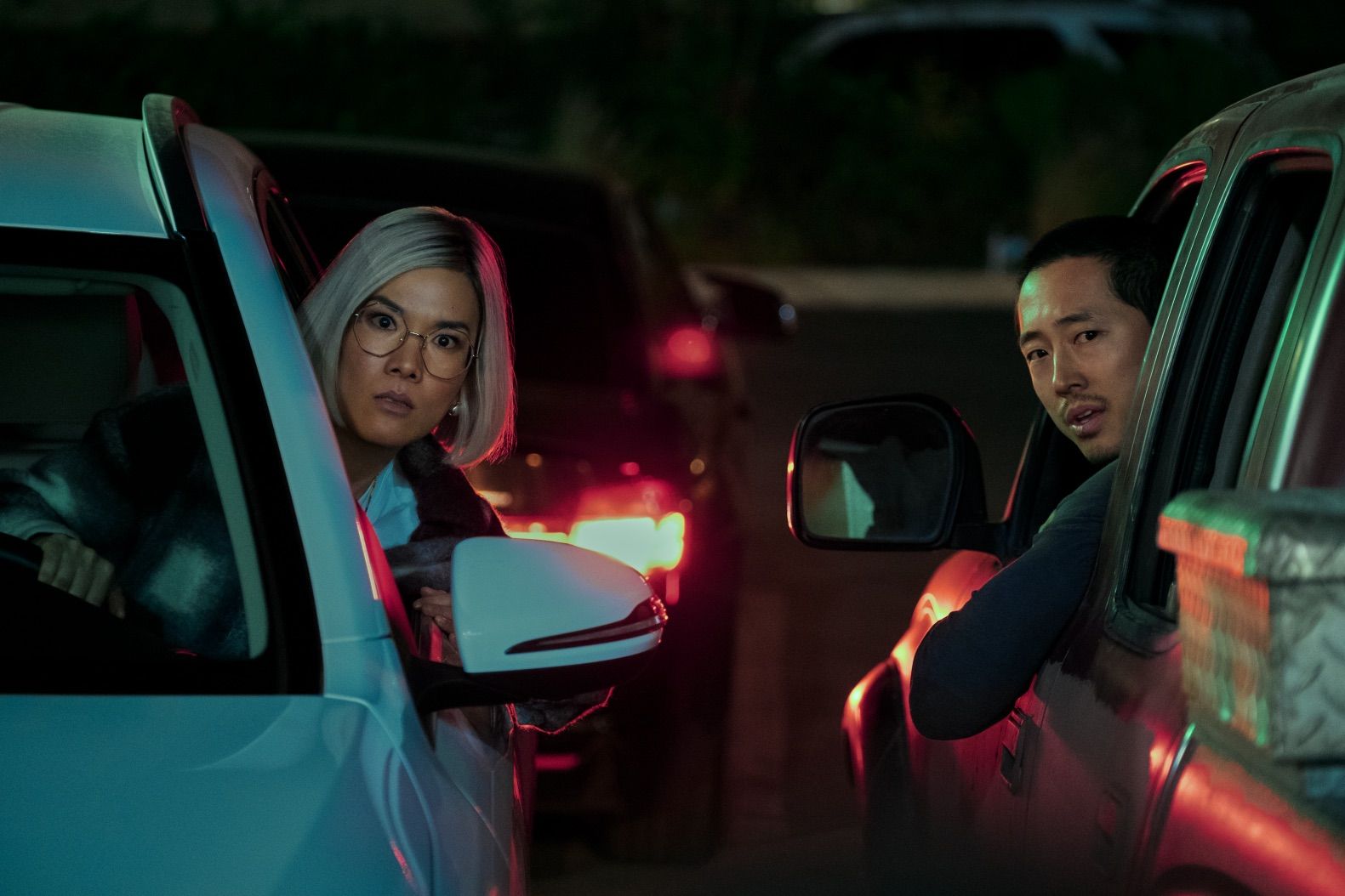 Ali Wong and Steven Yeun hang their heads outside car windows during an altercation.