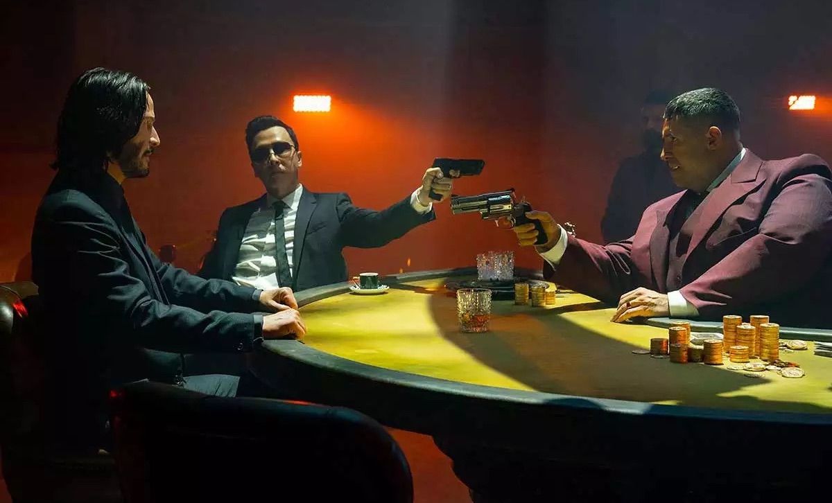 Seated around a poker table, three suited men point guns at each other during a tense game.